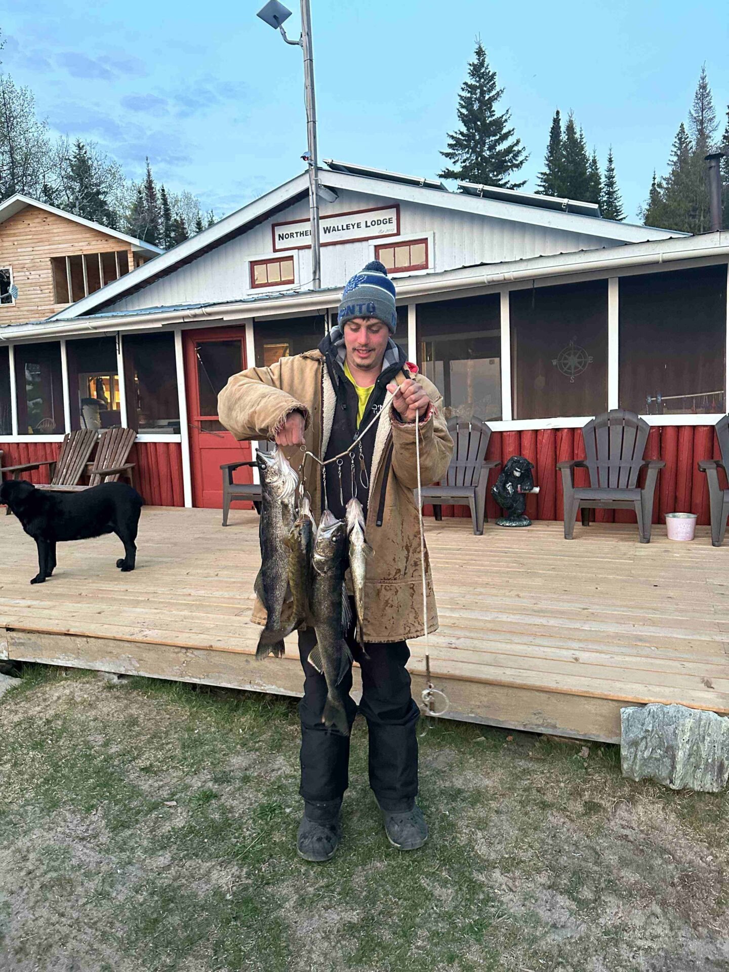 Devin holding two walleye on a stringer in front of the Northern Walleye Lodge building